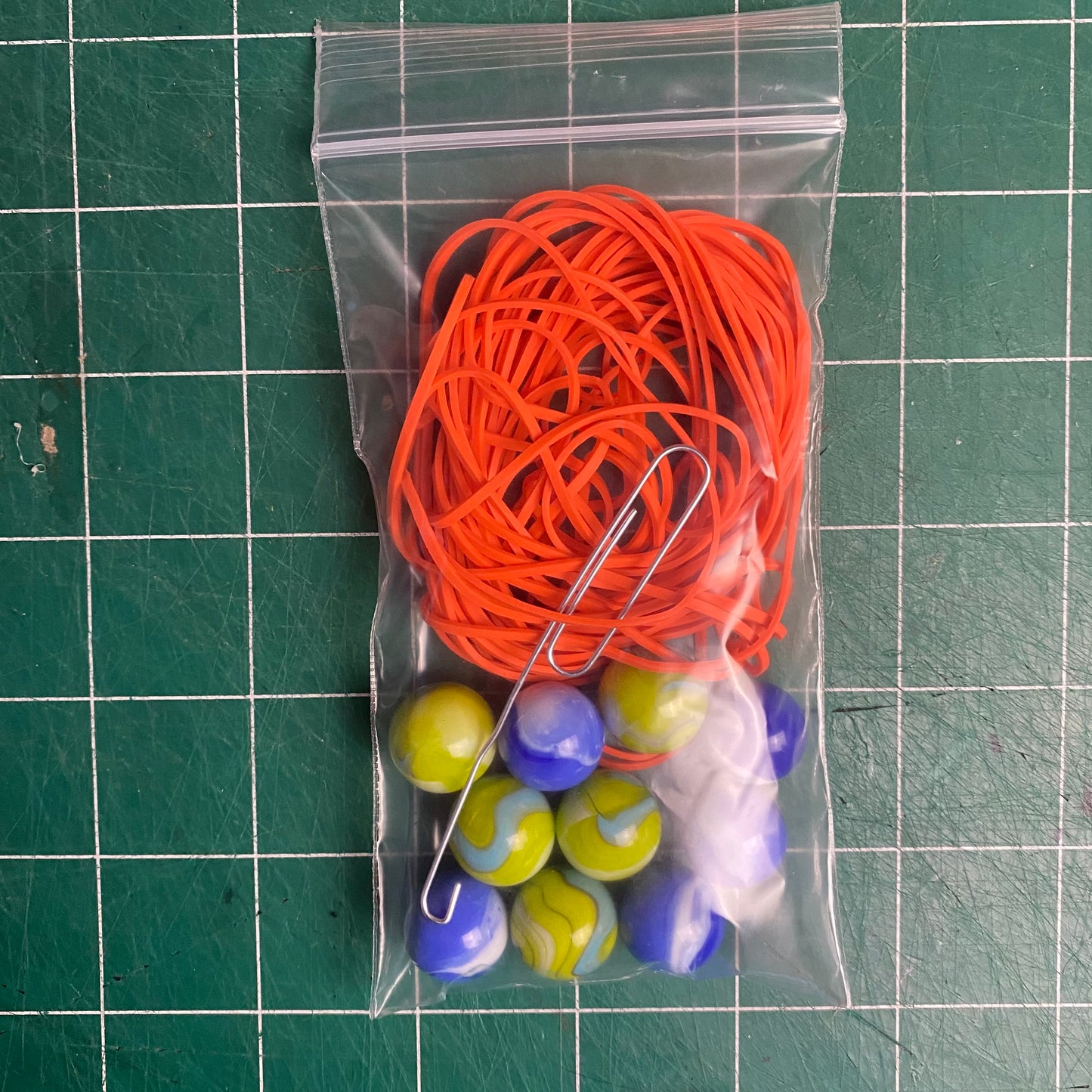 Small poly bag containing 40 rubber bands, 10 marbles, and a paper clip "hook tool"